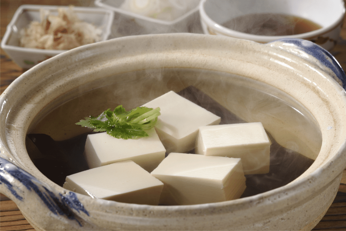 15 Irresistible Traditional Kyoto Foods You Need to Try 2 A steaming ceramic pot filled with hot water and several cubes of tofu, garnished with fresh greensāa classic example of Traditional Kyoto Dishes. Small dishes with condiments and sauce are blurred in the background.