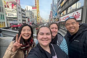 Four individuals posing for a selfie in an urban area with buildings and a canal in the background.