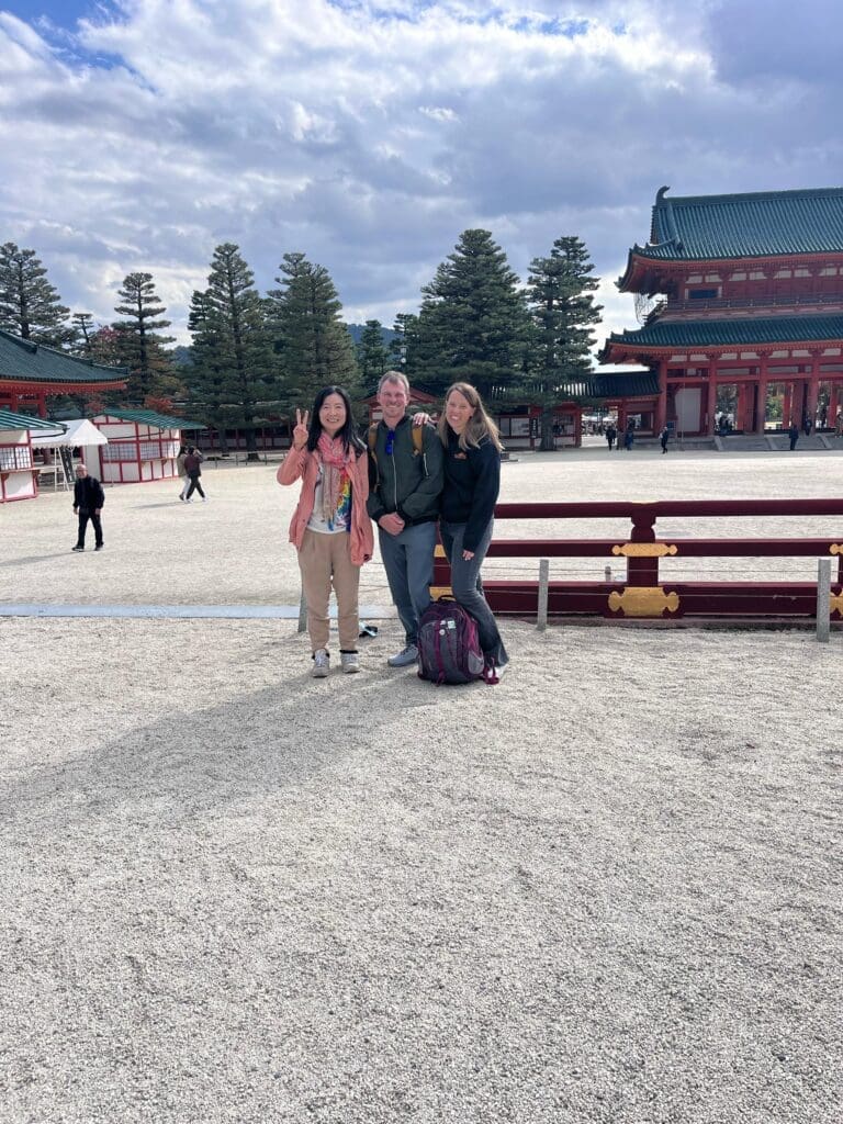 Three individuals posing together at Heian Shrine in Kyoto, Japan, with traditional architecture in the background.