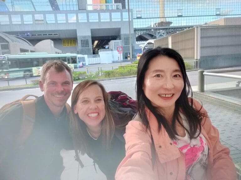 Three individuals posing for a selfie at a transportation hub, with a modern building in the background.