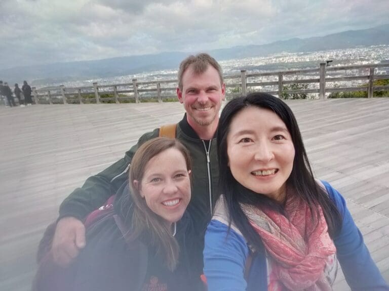 Three individuals posing for a selfie at a viewpoint with a cityscape in the background.